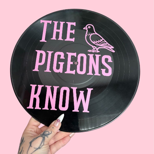 Vinyl record with 'The Pigeons Know' text and a pigeon illustration on a pink background